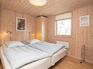 A double bed with a light-colored duvet, two bedside lamps, a window with a view, and wooden paneling on the walls. - 4 Star Holiday Home in Jerup (Jerup)