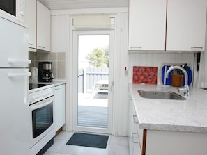 A compact kitchen with white cabinets, a built-in oven, a coffee maker, and a sink with a faucet.