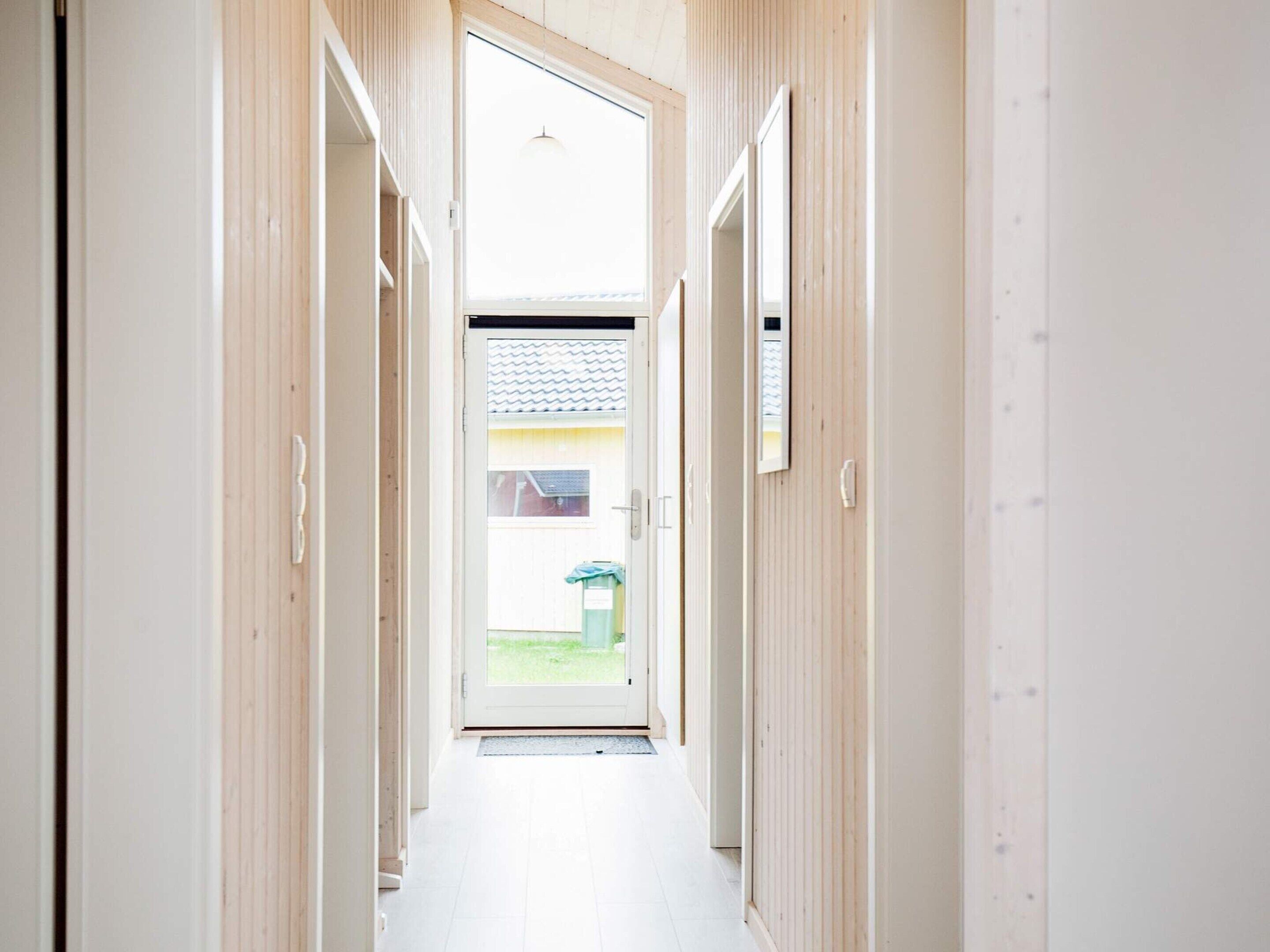 A narrow hallway with wooden paneling and a door leading to a bright room with a view of a garden.