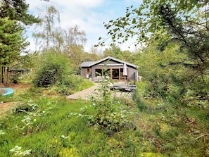 A cabin with a deck, surrounded by dense greenery. - 5 Person Holiday Home in Hemmet (Hemmet)