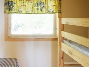 Uma cama beliche com janela acima, uma mesa xadrez e um cortinado com estampas de animais.
