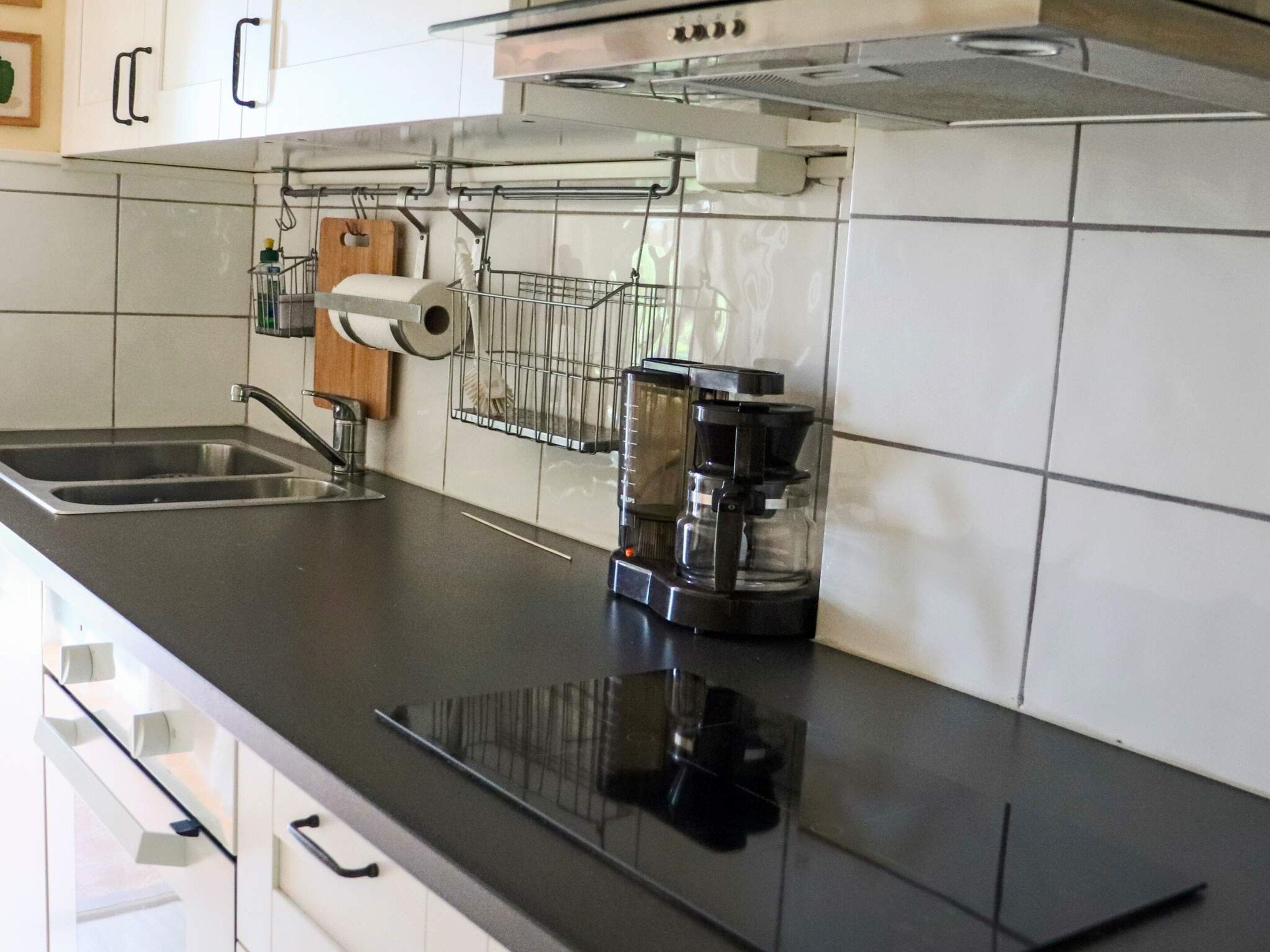 A kitchen with a black countertop, stainless steel sink, and a coffee maker.