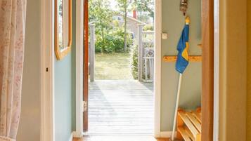 A doorway leading to a wooden deck with a view of a garden and a house in the background.