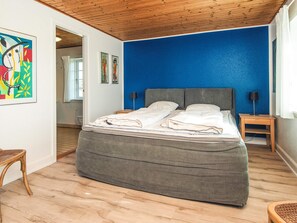 A bedroom with a large bed, wooden flooring, a blue accent wall, and artwork on the walls.