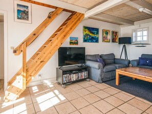 A living room with a wooden staircase, a flat-screen TV, a bookshelf, and a sofa. - 5 Star Holiday Home in Blavand (Blavand)