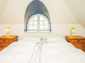 A bedroom with a large bed, two bedside tables with lamps, a window with an arch, and a sloped ceiling.