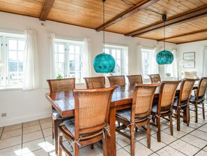 A dining area with a wooden table and chairs, large windows, and a wooden ceiling. - 5 Star Holiday Home in Blavand (Blavand)