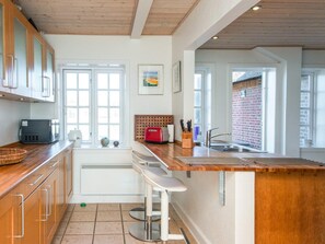 A kitchen with wooden cabinets, a built-in microwave, a red toaster, and a large window. - 5 Star Holiday Home in Blavand (Blavand)