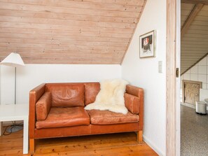 A brown leather sofa with a white fur throw, a white floor lamp, and a framed picture on the wall. - 5 Star Holiday Home in Blavand (Blavand)