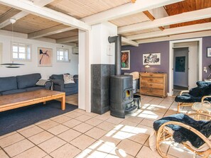 A cozy living room with a fireplace, a sofa, a coffee table, and wicker chairs. - 5 Star Holiday Home in Blavand (Blavand)