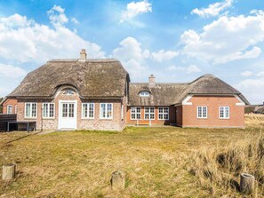 A traditional brick house with a thatched roof, a white door, and multiple windows.