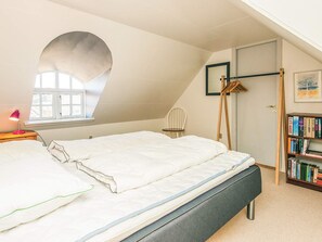 A bedroom with a bed, a window, a chair, a bookshelf, and a door. - 5 Star Holiday Home in Blavand (Blavand)