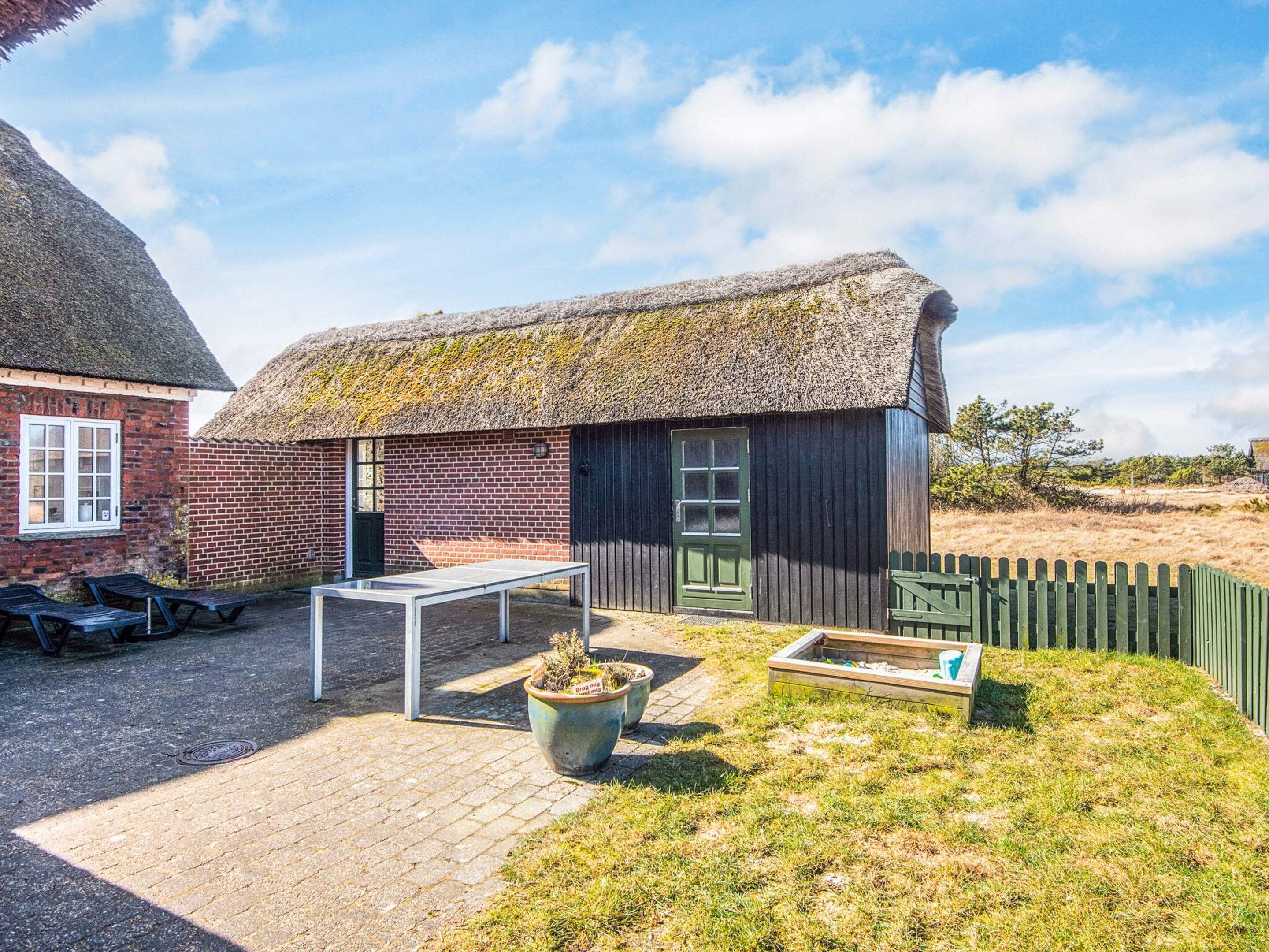 Un bâtiment à toit de chaume, avec une façade en briques, une porte en bois et une petite fenêtre.