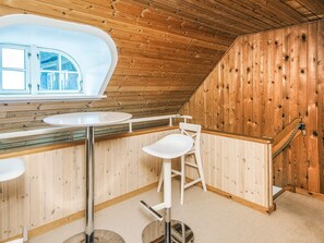 A wooden interior with a high ceiling, a window with a view, a white bar area with stools, and a staircase.