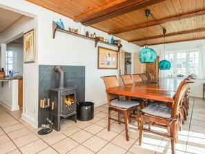 A dining area with a wooden table and chairs, a stone fireplace, and a hanging light fixture.