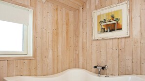 A bathroom with a freestanding bathtub, wooden panel walls, a window, and a framed picture on the wall. - Quaint Holiday Home in LÃ¸kken near Beach (Lokken)