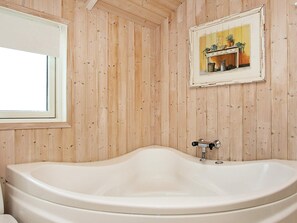 A bathroom with a freestanding bathtub, wooden panel walls, a window, and a framed picture on the wall. - Quaint Holiday Home in LÃ¸kken near Beach (Lokken)