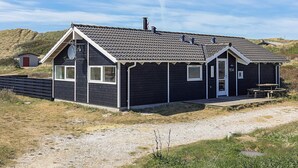 A two-story building with a dark exterior, a red door, and a small attached structure. - Quaint Holiday Home in LÃ¸kken near Beach (Lokken)