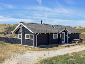 A two-story building with a dark exterior, a red door, and a small attached structure. - Quaint Holiday Home in LÃ¸kken near Beach (Lokken)