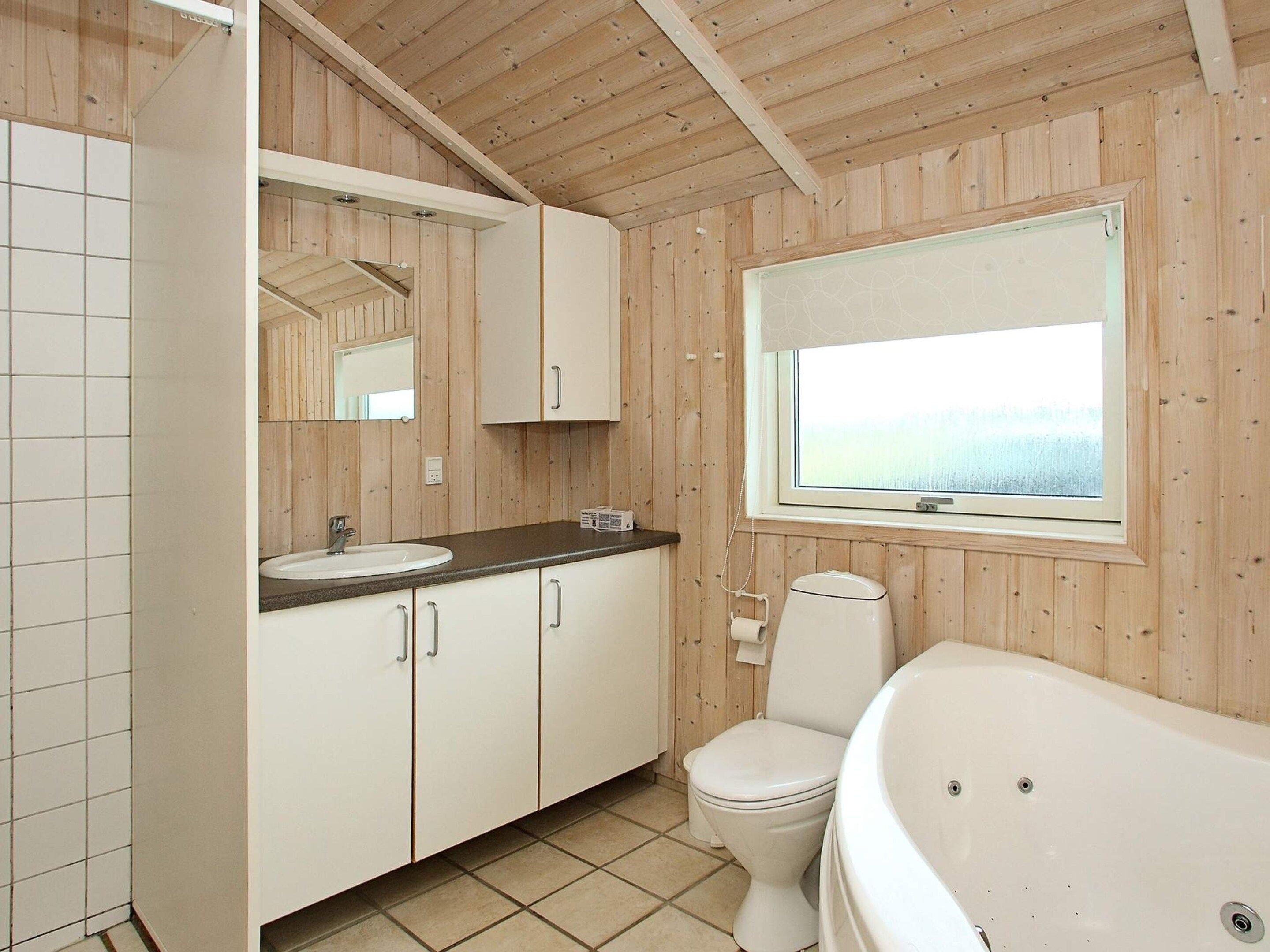 Een badkamer met een houten inrichting, een witte wastafel, een toilet en een bad.