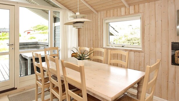 A wooden dining area with a table and chairs, a hanging light fixture, a window with a view, and a door leading outside. - Quaint Holiday Home in LÃ¸kken near Beach (Lokken)