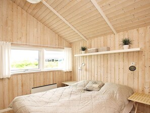 A bedroom with a bed, a window, a shelf with plants, and a wall-mounted lamp.