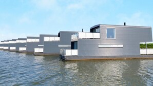 A modern floating building with a flat roof, large windows, and a water barrier.