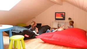 Una habitación acogedora en el desván con techo inclinado, un televisor en la pared y suelo de madera.