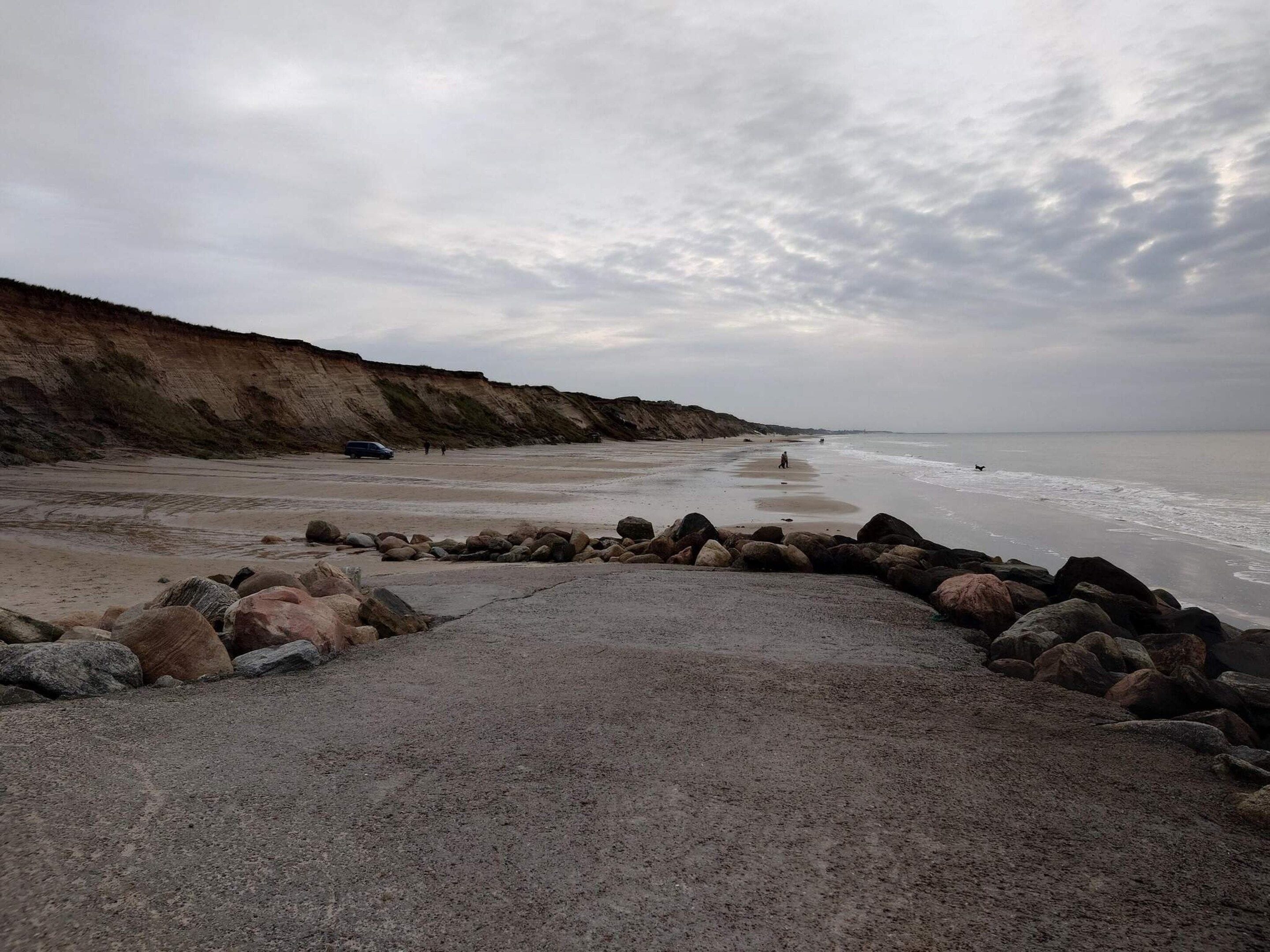 Ein Strand mit felsigem Vordergrund, einer Klippe und dem Meer im Hintergrund.