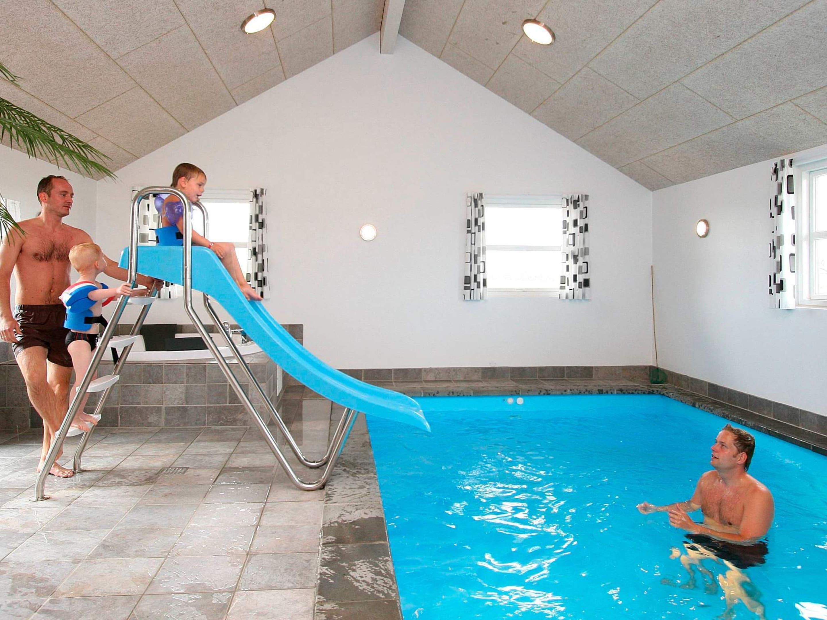 An indoor swimming pool with a slide, tiled floor, and windows.