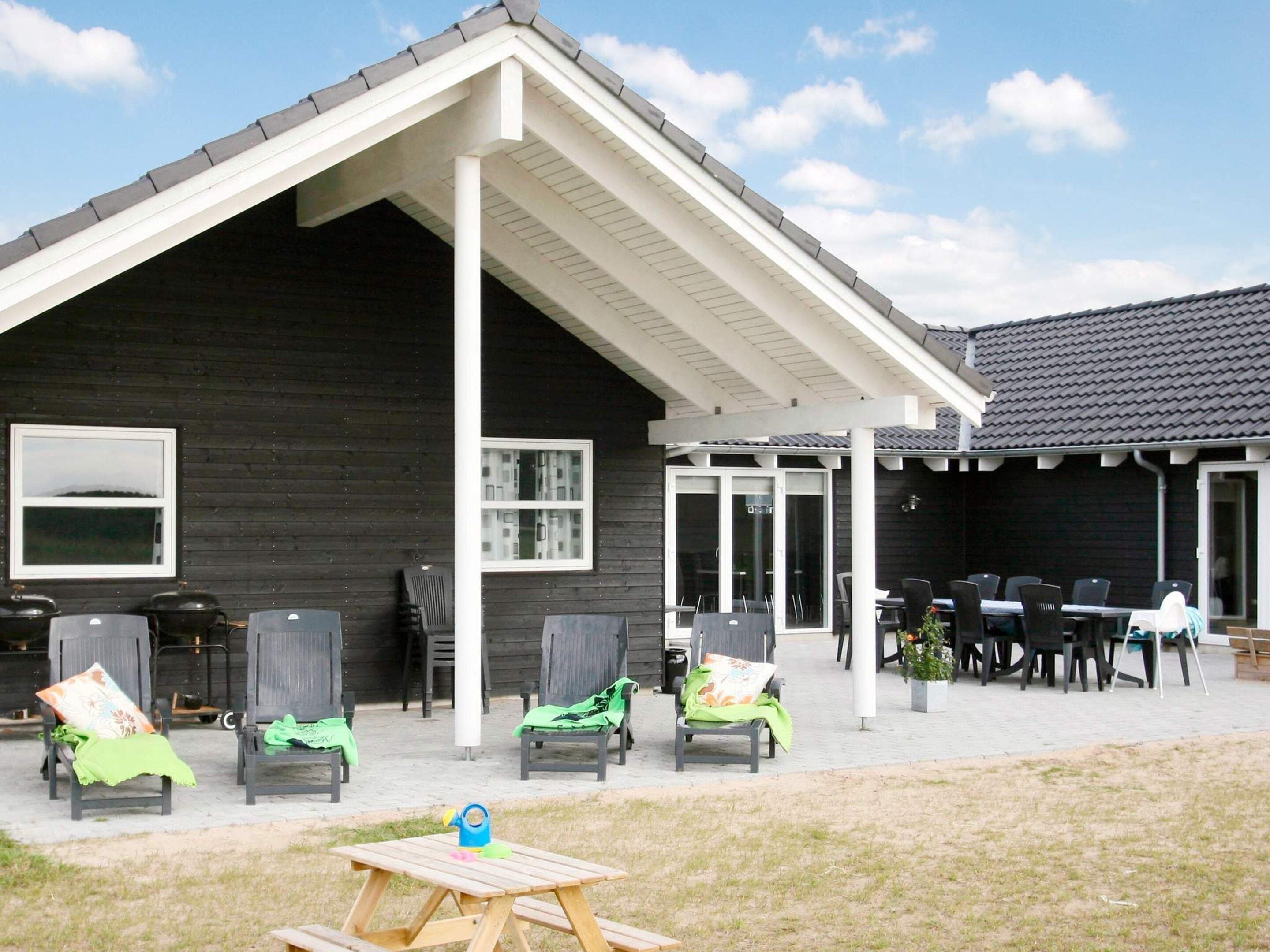 En bygning med en overdækket terrasse med udendørs siddepladser og et bord.