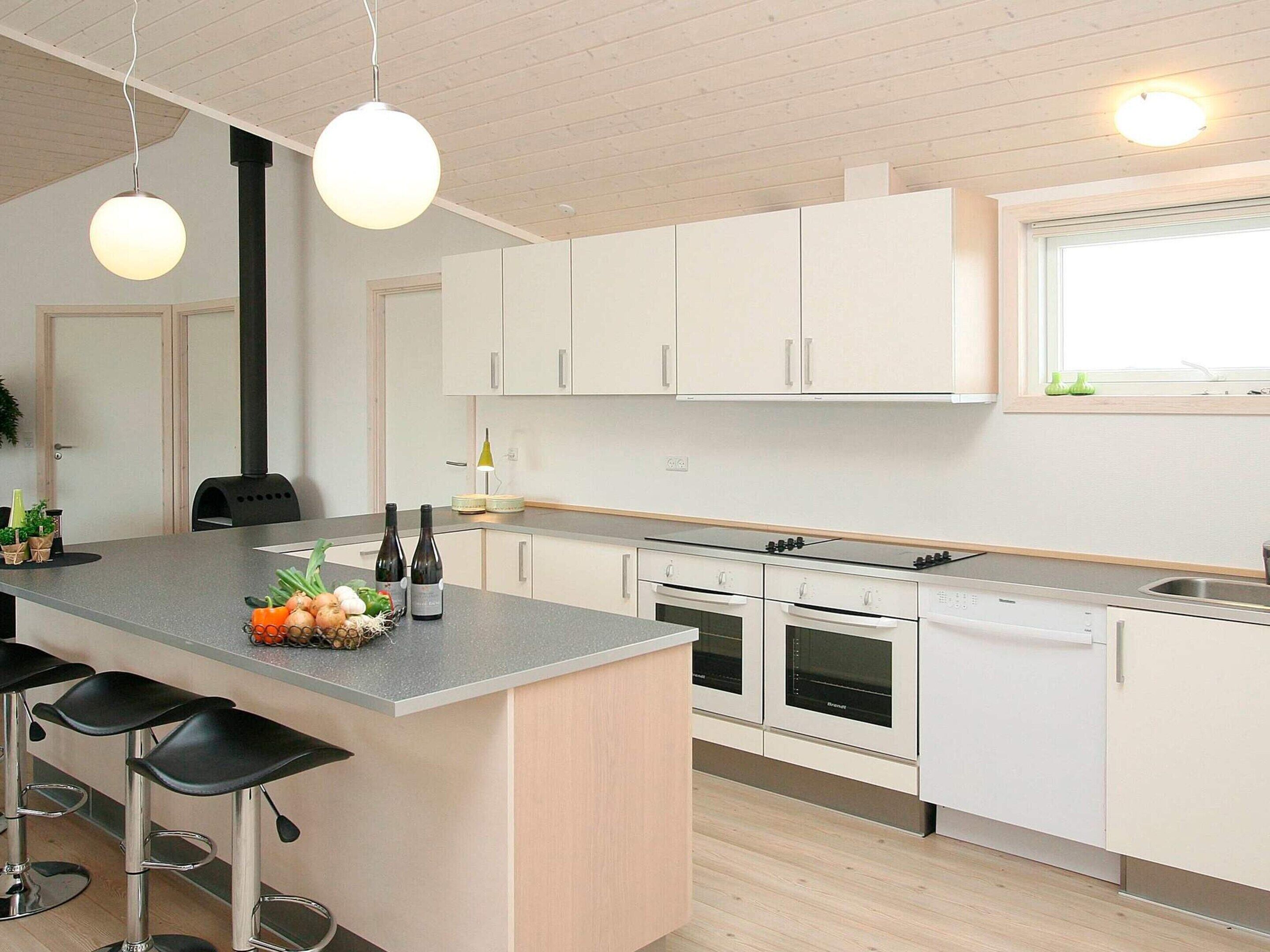 Et moderne køkken med hvide skabe, en central ø med barstole, indbygget ovn og komfur.