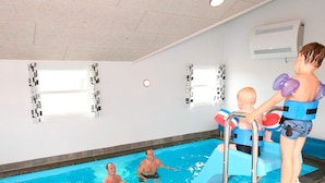 Una piscina interior con una escalera, un niño con un dispositivo flotador y dos adultos.
