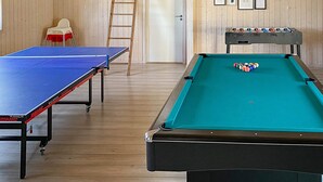 Una sala de billar con mesa de billar, mesa de futbolín y mesa de ping pong.