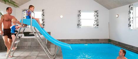An indoor swimming pool with a slide, tiled walls, and a high ceiling.