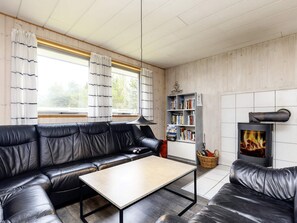A cozy living room with a black leather sofa, a wooden coffee table, a bookshelf, and a fireplace. - Enticing Holiday Home in Falster near Sea (Vaeggerlose)