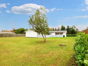 A white building with a sloped roof, surrounded by a grassy yard and a wooden fence. - Enticing Holiday Home in Falster near Sea (Vaeggerlose)