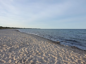 A sandy beach with gentle waves, a clear sky, and a distant shoreline.