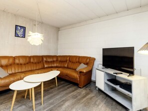 Un salon moderne avec un canapé d’angle en cuir marron, une table basse blanche, un téléviseur à écran plat posé sur un meuble blanc et un luminaire suspendu.