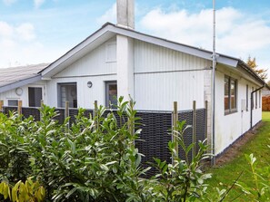 A white building with a sloped roof, a chimney, and a fenced area with green shrubs. - Enticing Holiday Home in Falster near Sea (Vaeggerlose)