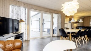 Un salon moderne doté d’un téléviseur à écran plat, d’un canapé en cuir, d’un coin repas avec des chaises et d’une grande fenêtre agrémentée de rideaux.