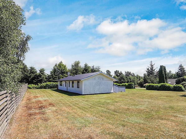 A single-story white building with a dark roof, surrounded by a well-maintained lawn and a wooden fence.