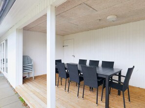 A covered outdoor dining area with a table and chairs, a stack of chairs, and a door. - Enticing Holiday Home in Falster near Sea (Vaeggerlose)