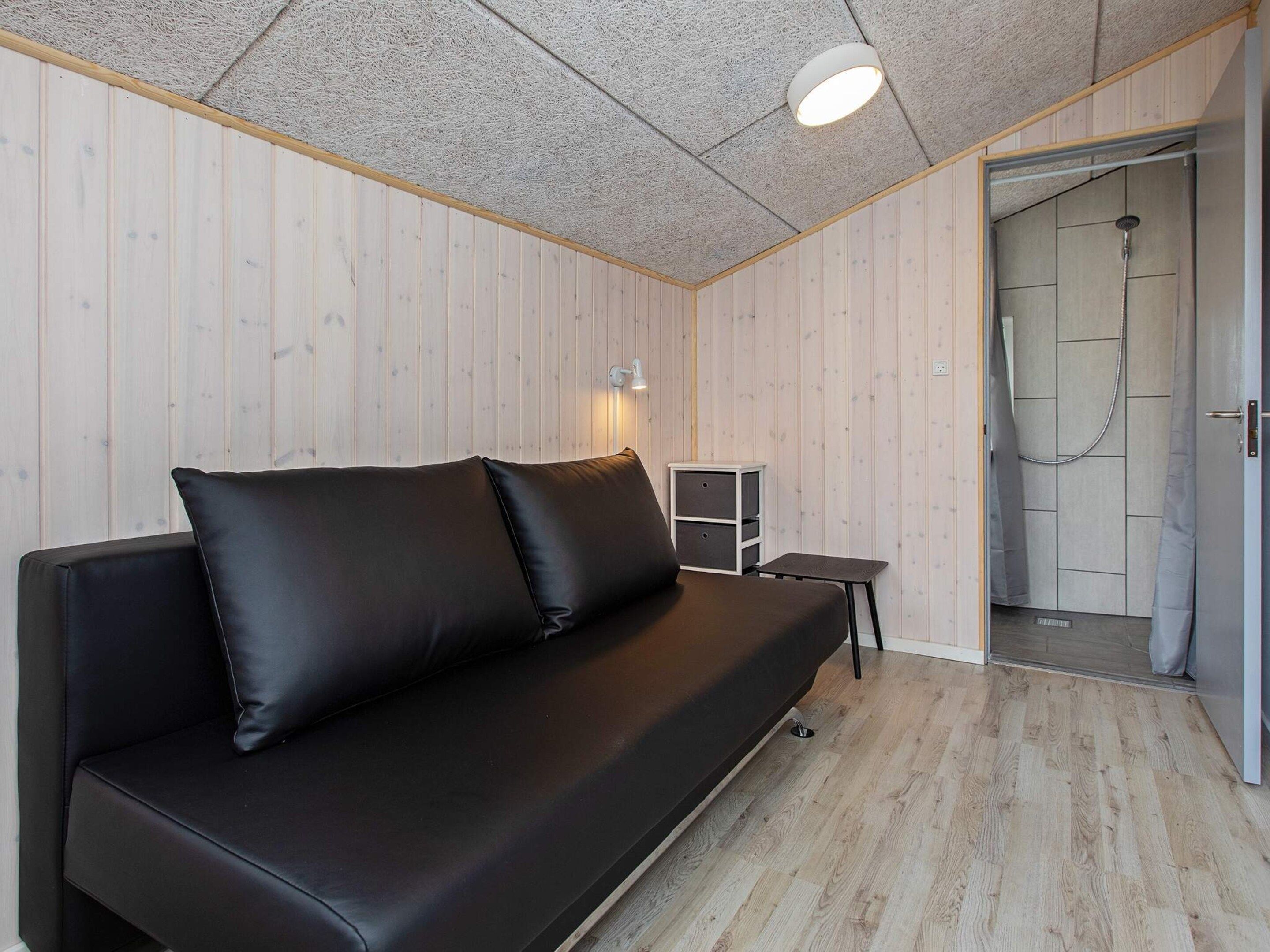 Et værelse med en sort lædersofa, et lille bord, et skab og et bruseområde.