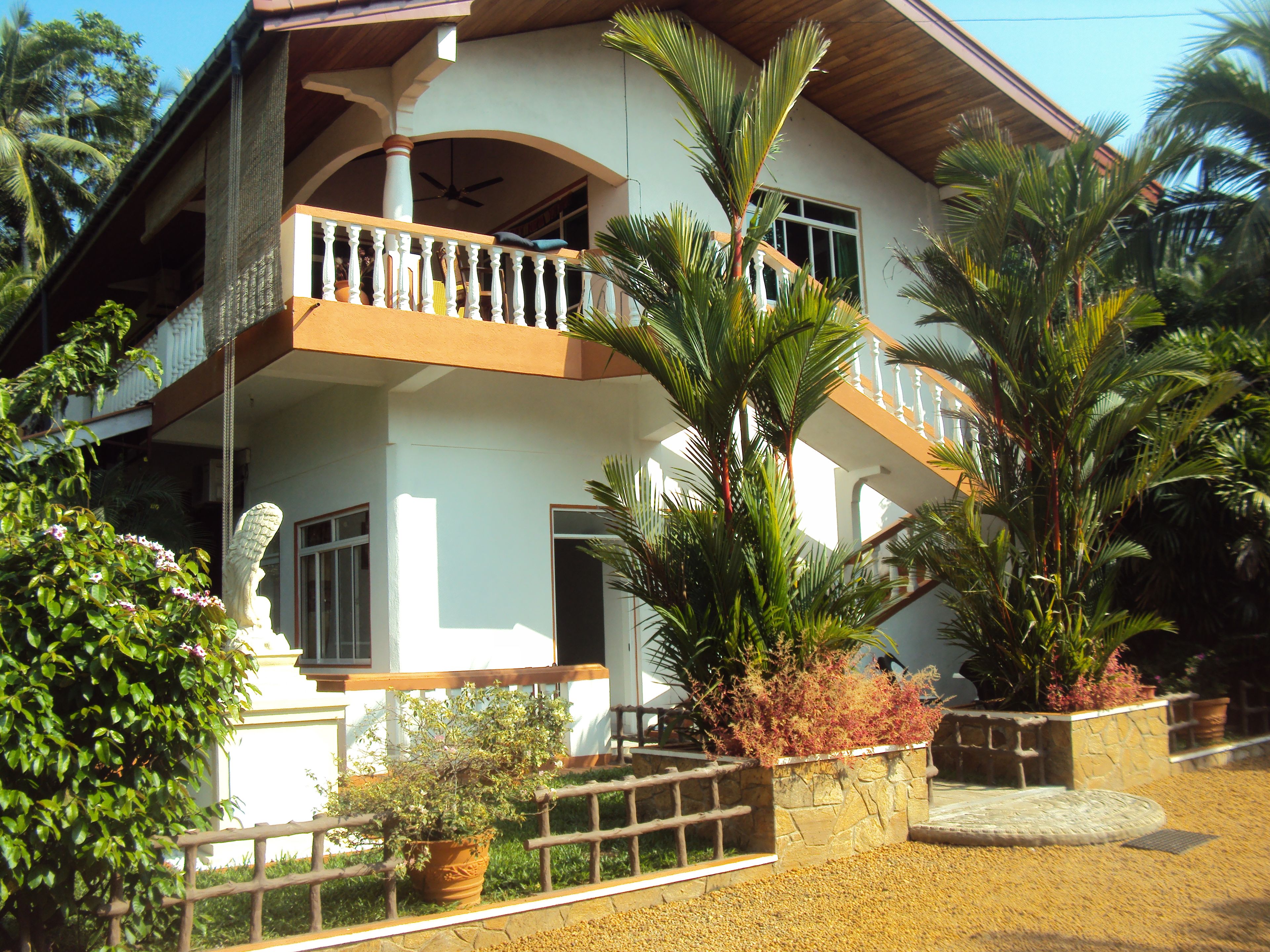 A two-story house with a balcony, surrounded by tropical plants.