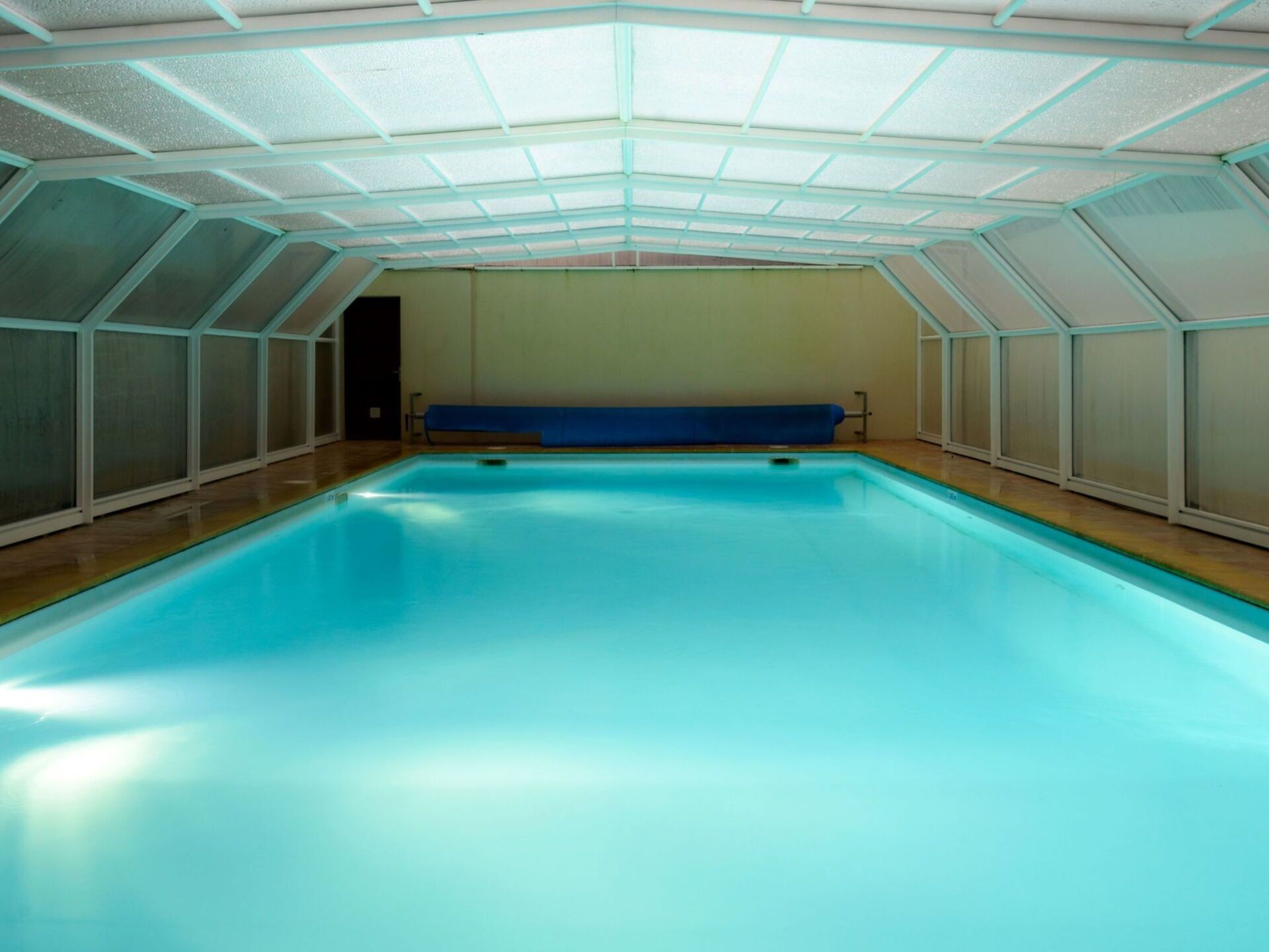 An indoor swimming pool with a blue floor, surrounded by walls with a geometric pattern.