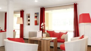 A modern hotel room with wicker furniture, red cushions, and a view of the sea. - Nice apartment for 4 people with pool, WIFI, TV, terrace and pets allowed (Le Carquois)