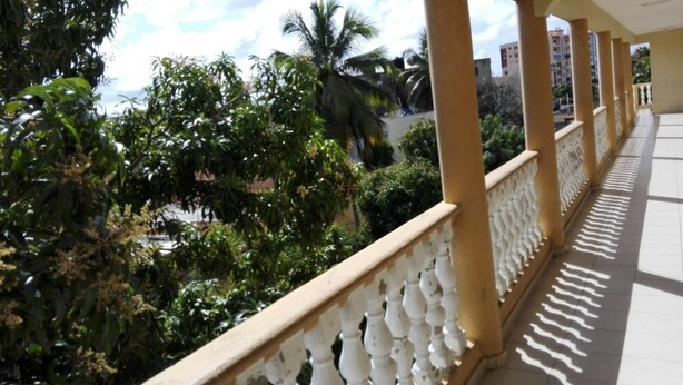 A balcony with a white balustrade, lush greenery, and a clear sky. - Bright and Youth Condo With hot Water (Santo Domingo Este)