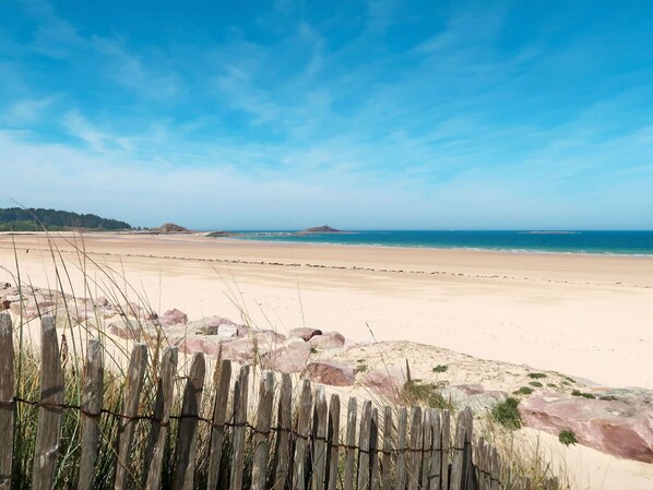A beach with a wooden fence in the foreground, a sandy shore, and a clear blue sky.
