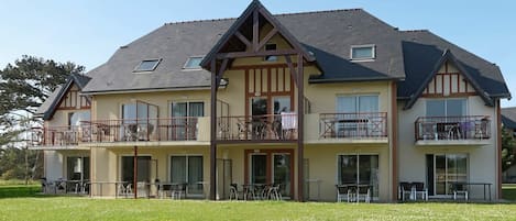 A two-story building with balconies, large windows, and a grassy lawn.